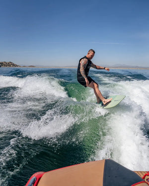 Black | Black competition wake surf vest in lifestyle image surfing the  Keowee board behind a G23 Nautique. 