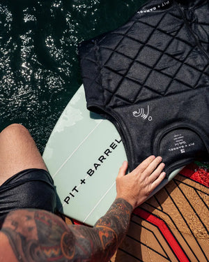  Lifestyle detail image of black wake surf  competition impact vest in water next to wake surf board. 