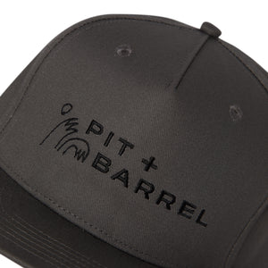Detail view of dark gray 5 panel snapback cap with 'Pit + Barrel' logo on a white background with high five curling wave. 