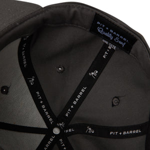 Detail view of inside of 5 panel snapback dark grey hat with 'pit and barrel' seam tape with 'Quality Surf' tag. 
