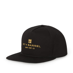 front 3/4 view of a Black 5 panel snapback cap with gold text 'pit + barrel wake surf co' and curling wave logo on a white background