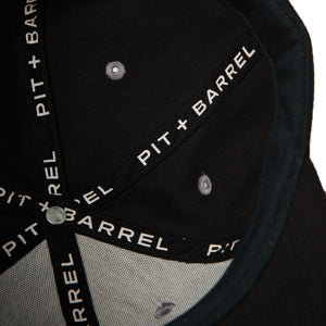 Detail  interior view of black 5 panel snapback cap with custom seam tape with text that says 'Pit + Barrel'.