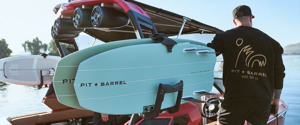 Man standing with Pit and Barrel high five sweatshirt with two Keowee boards on board racks at the dock on the Super Air Nautique G23 in red. 