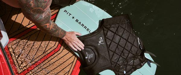 Lifestyle image of man sitting on back deck of wake surf boat with Wake Surf Board and Impact vest both from Pit and Barrel Surf. 