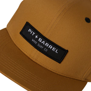 detail view of tan 6 panel cap with black 'pit + barrel wake surf co' logo.