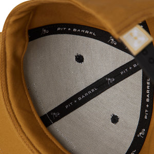 detail view of tan 6 panel cap with black 'pit + barrel' text on inside tape seams with 'high five' wave curl logo. 