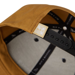 detail view of tan 6 panel cap with wave curl logo. 