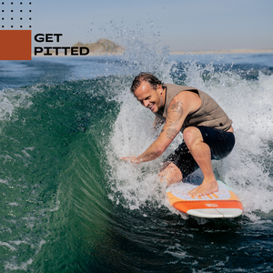 A person riding a retro wakesurf board on a curling wave, crouched low with one hand skimming the water. The rider wears a tan competition impact life vest and black shorts, and the board has an orange and white nose. Water sprays dramatically around them, and the background shows open water and distant shoreline. The text ‘GET PITTED’ appears in the top left.