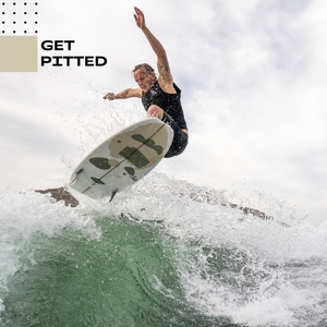 Lifestyle image of pro surfer getting air on wave on the 'high five' wake surf board wearing the slasher competition impact vest in black and side zip. 